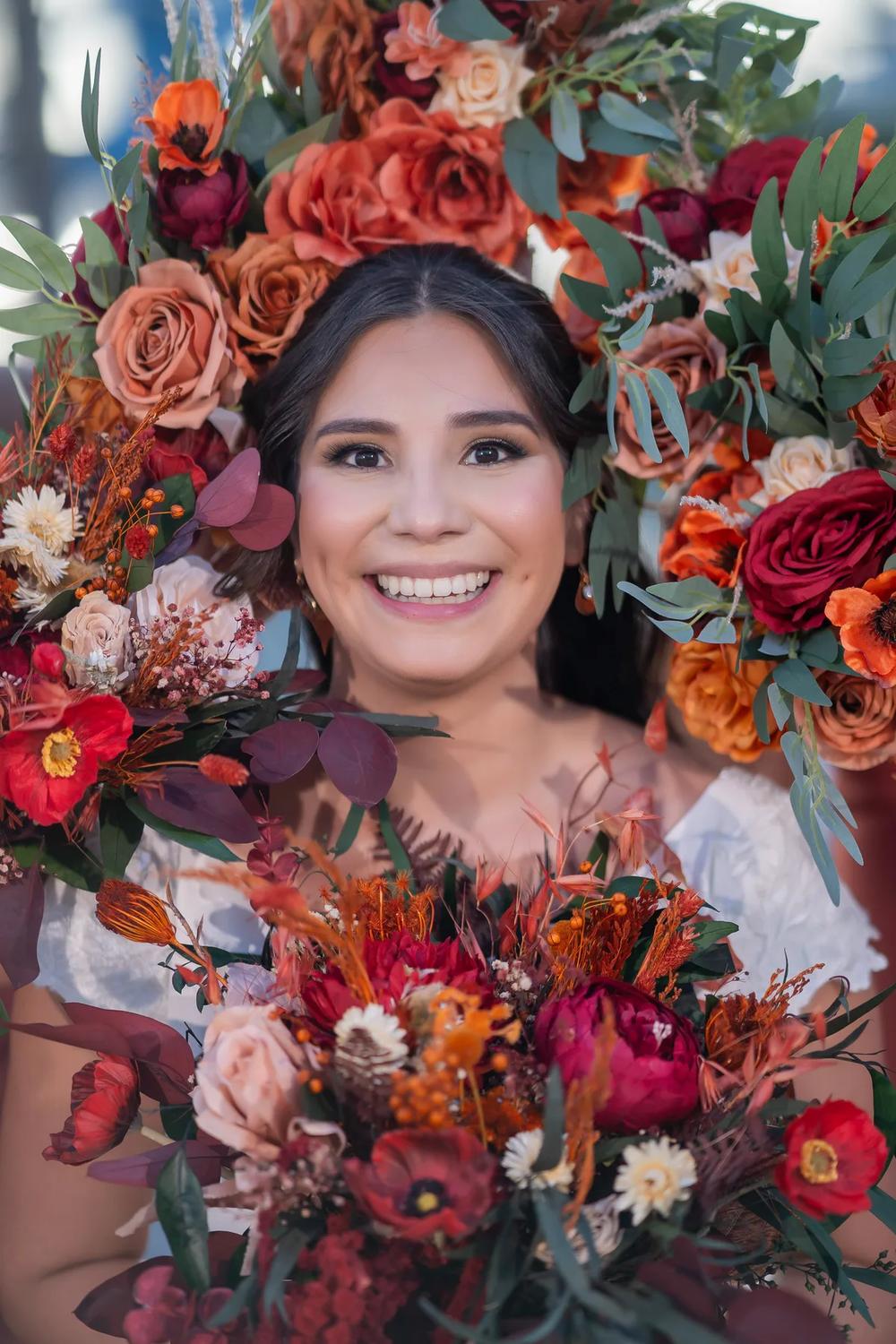 A radiant bride smiles amidst a vibrant floral arrangement in an outdoor setting during golden hour.