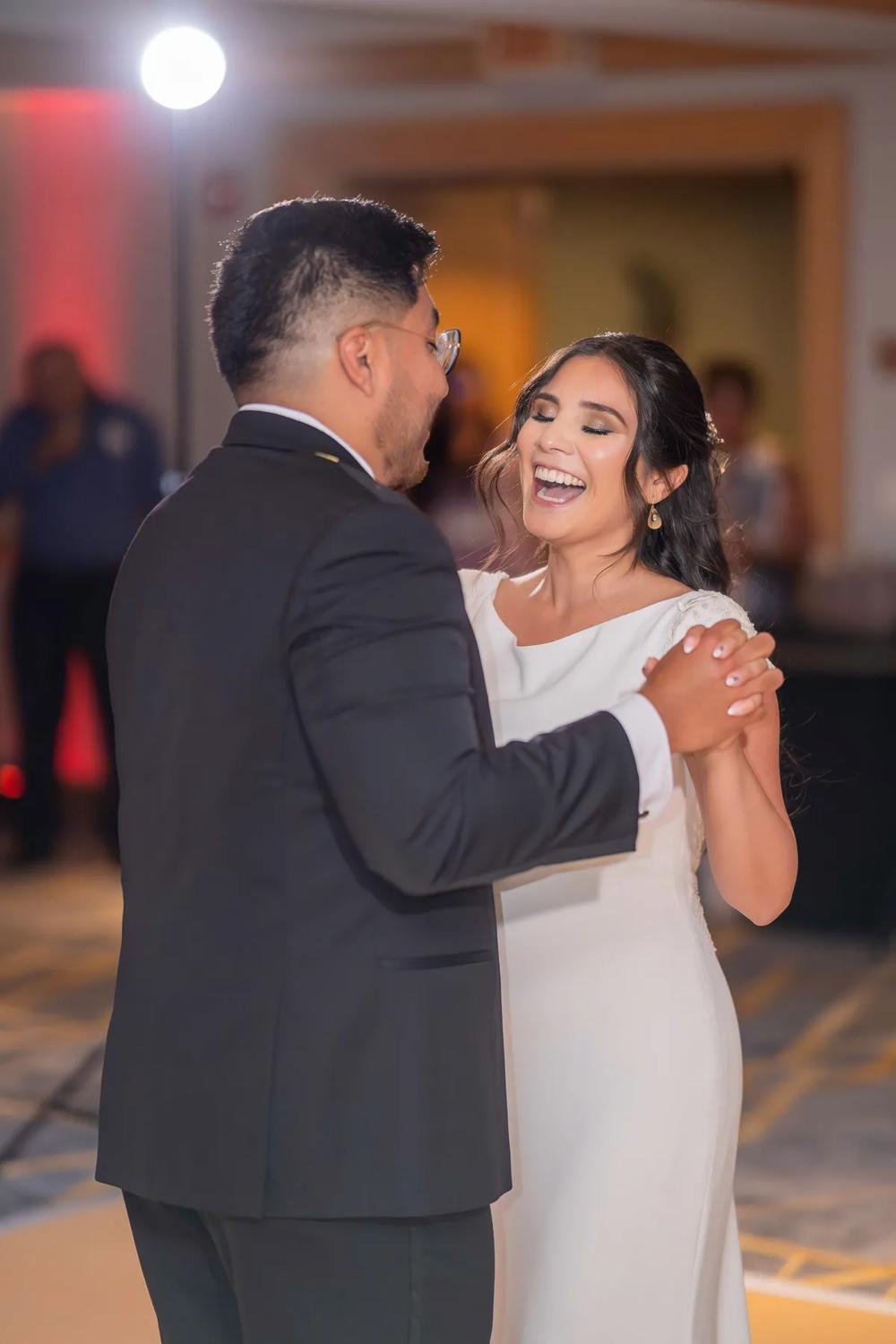 A joyful bride and groom share a dance under warm stage lighting at their wedding reception.