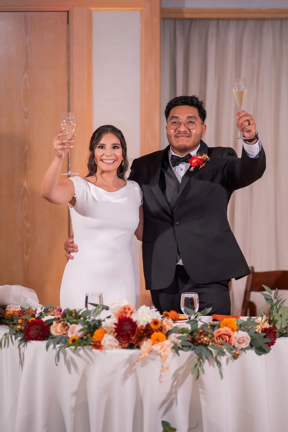 A bride and groom raise their champagne glasses in a toast at their wedding reception.