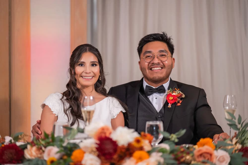 A bride and groom share a joyful moment at their wedding reception with elegant table settings and warm lighting.