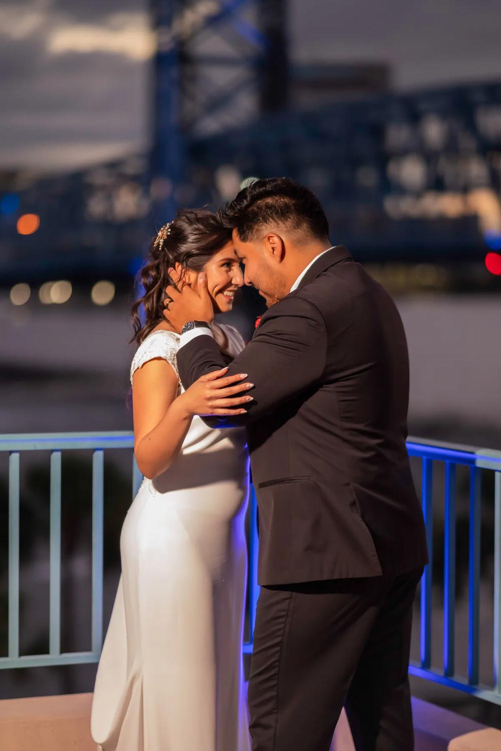 A bride and groom share an intimate moment on a waterfront deck at dusk.