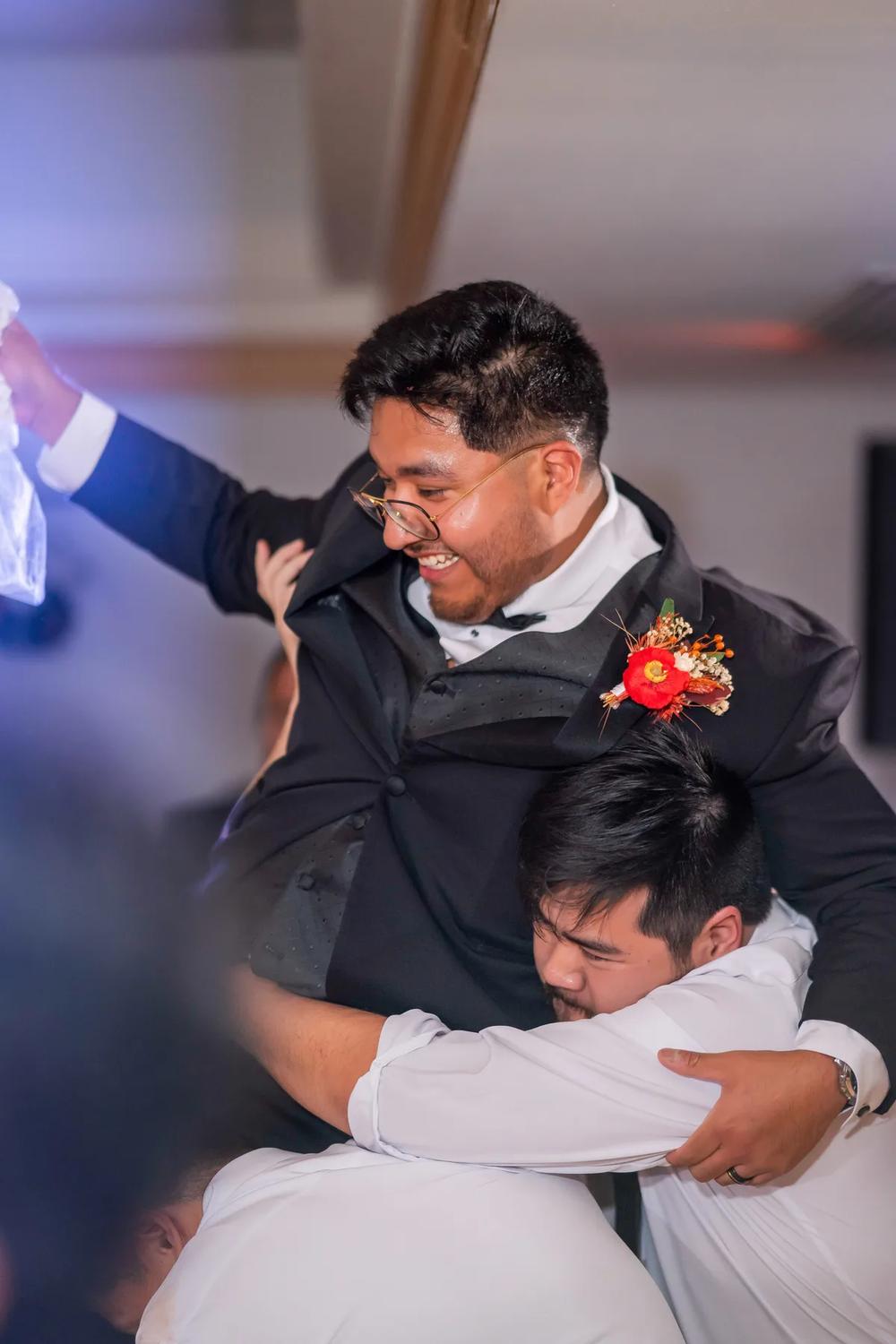 A groom is lifted joyfully by his friends during a lively wedding reception.