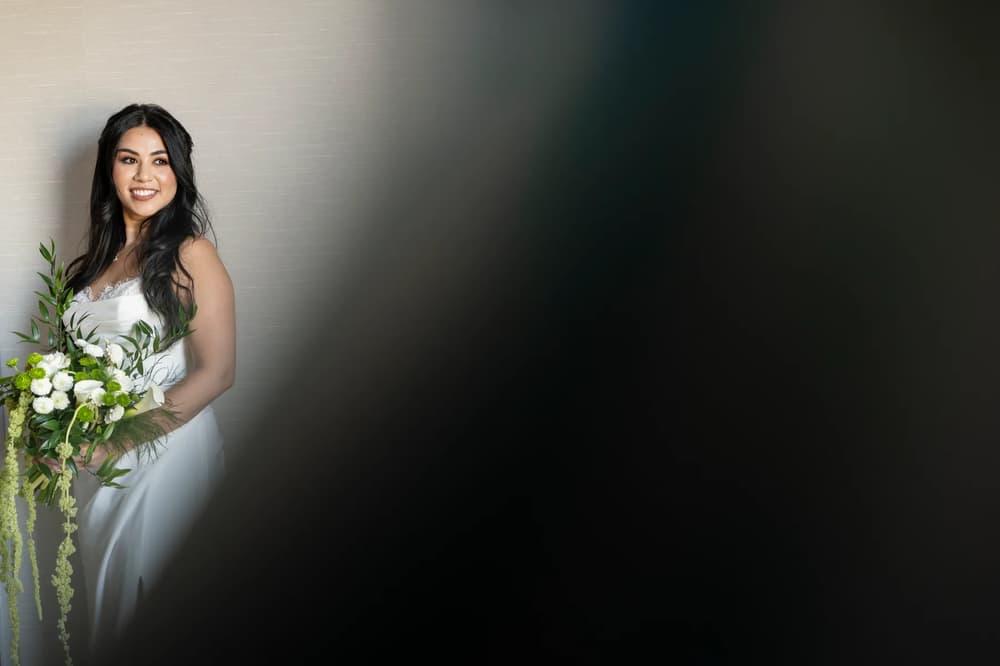 A woman wearing a white dress with flowers on her arm poses for the camera.