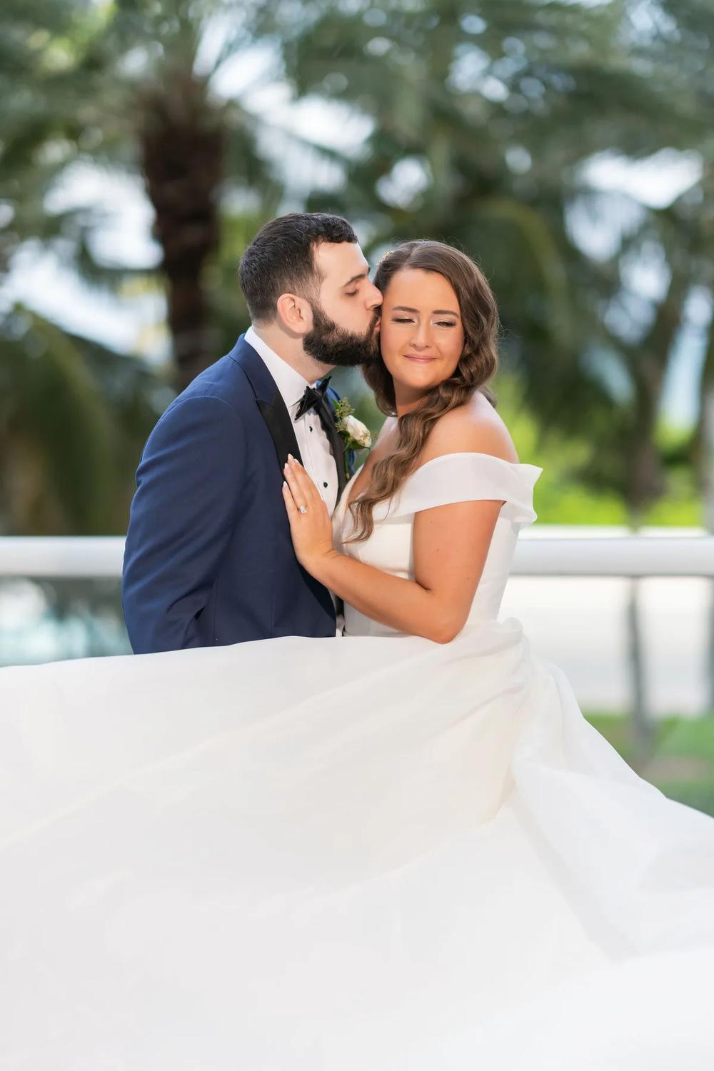 A tender moment between a bride and groom in an outdoor setting with palm trees, captured during the golden hour.