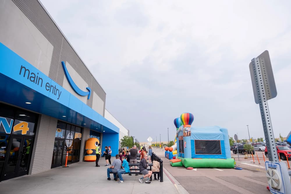 A lively outdoor gathering with inflatable bouncy castles and people enjoying the event outside an Amazon fulfillment center on a cloudy day.