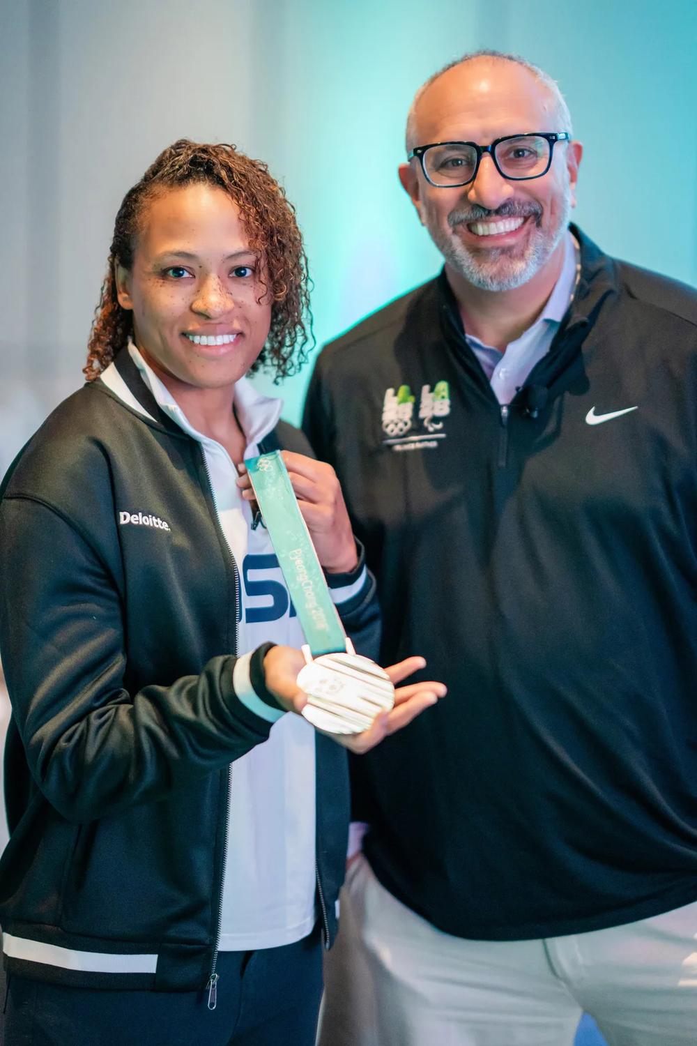 two athletes pose for a photo holding an Olympic medal.