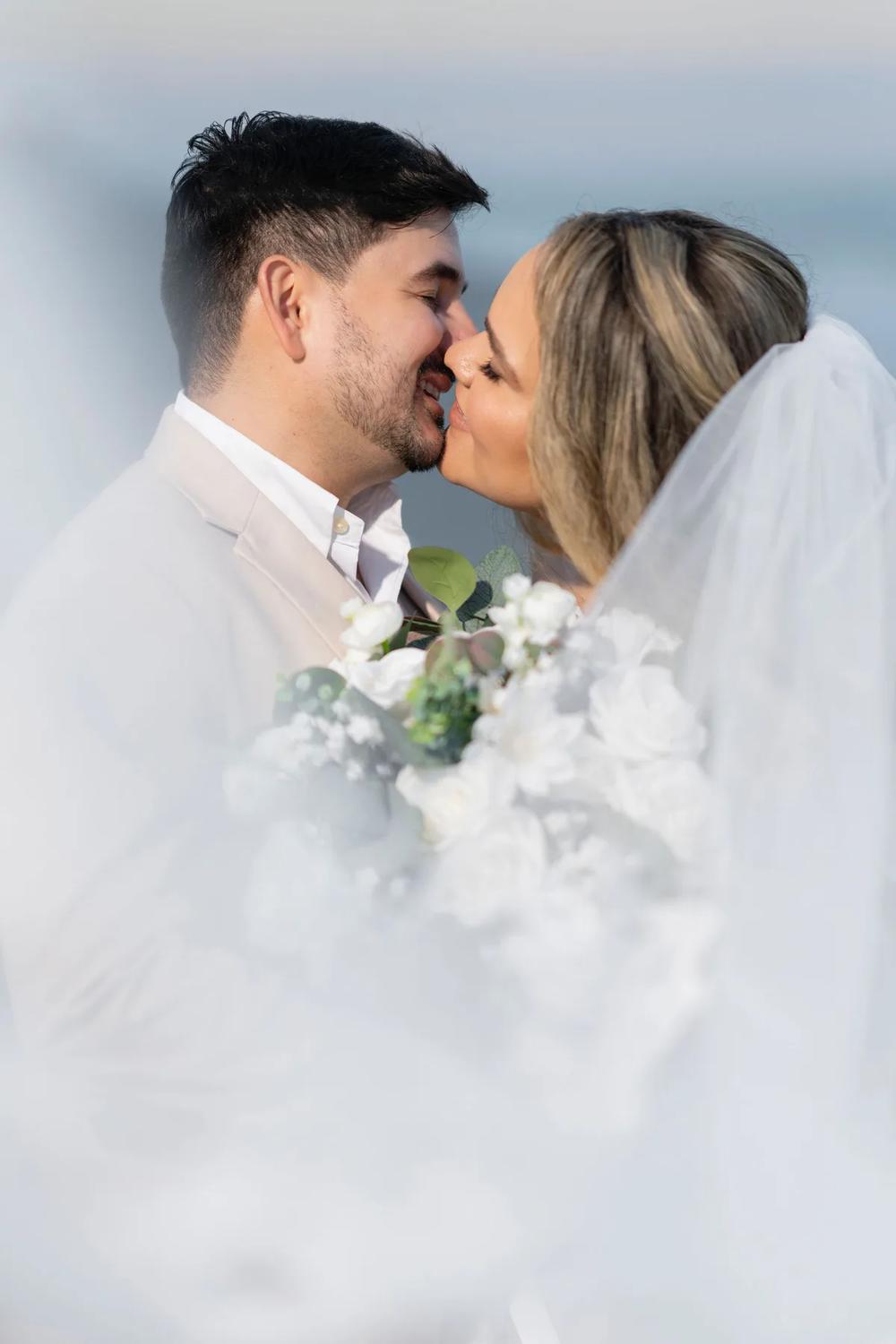 A bride and groom share a tender kiss against a soft, ethereal backdrop of misty clouds during golden hour.