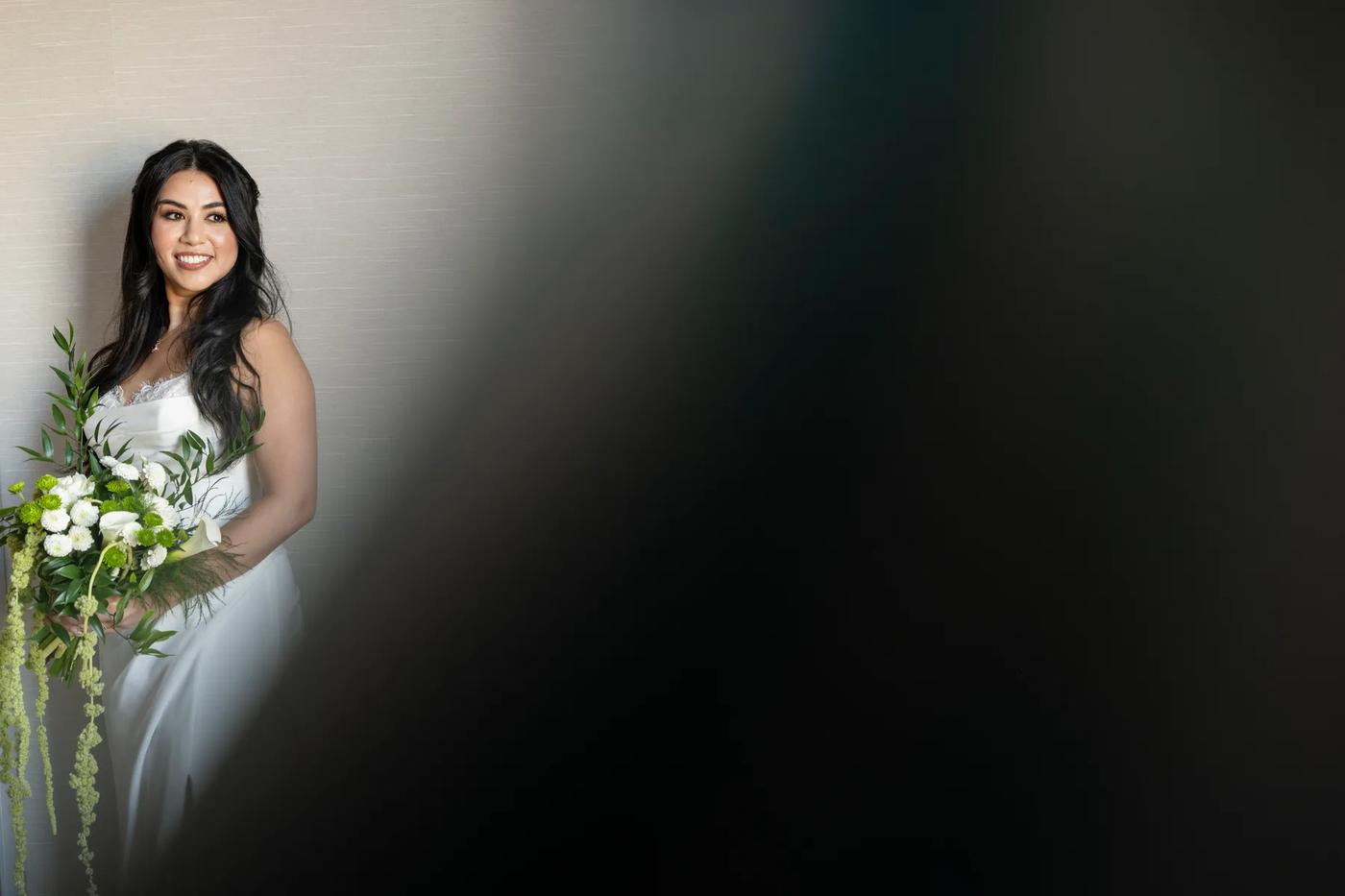 A woman wearing a white dress with flowers on her arm poses for the camera.