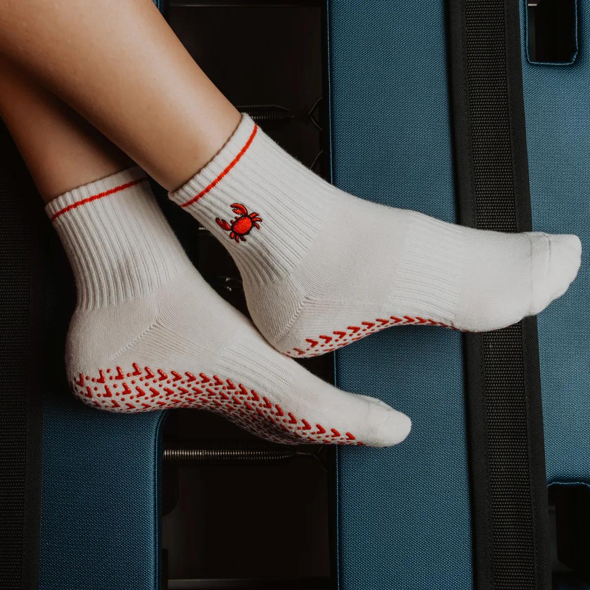 a close-up of feet wearing white socks with a red crab and textured soles, resting on the edge of an open suitcase.