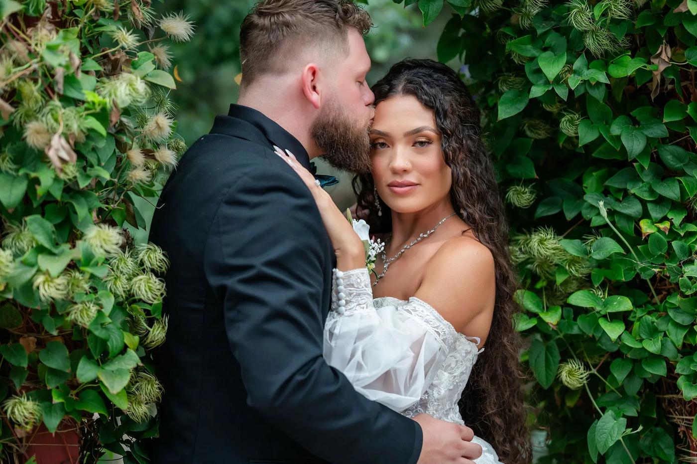 A bride and groom share an intimate moment amidst lush greenery in a serene outdoor garden setting.