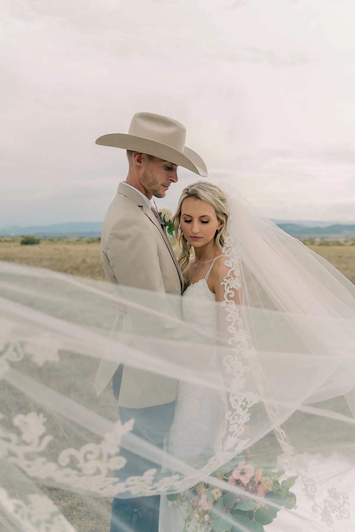 A bride and groom share a tender moment under an expansive sky in a rural setting.