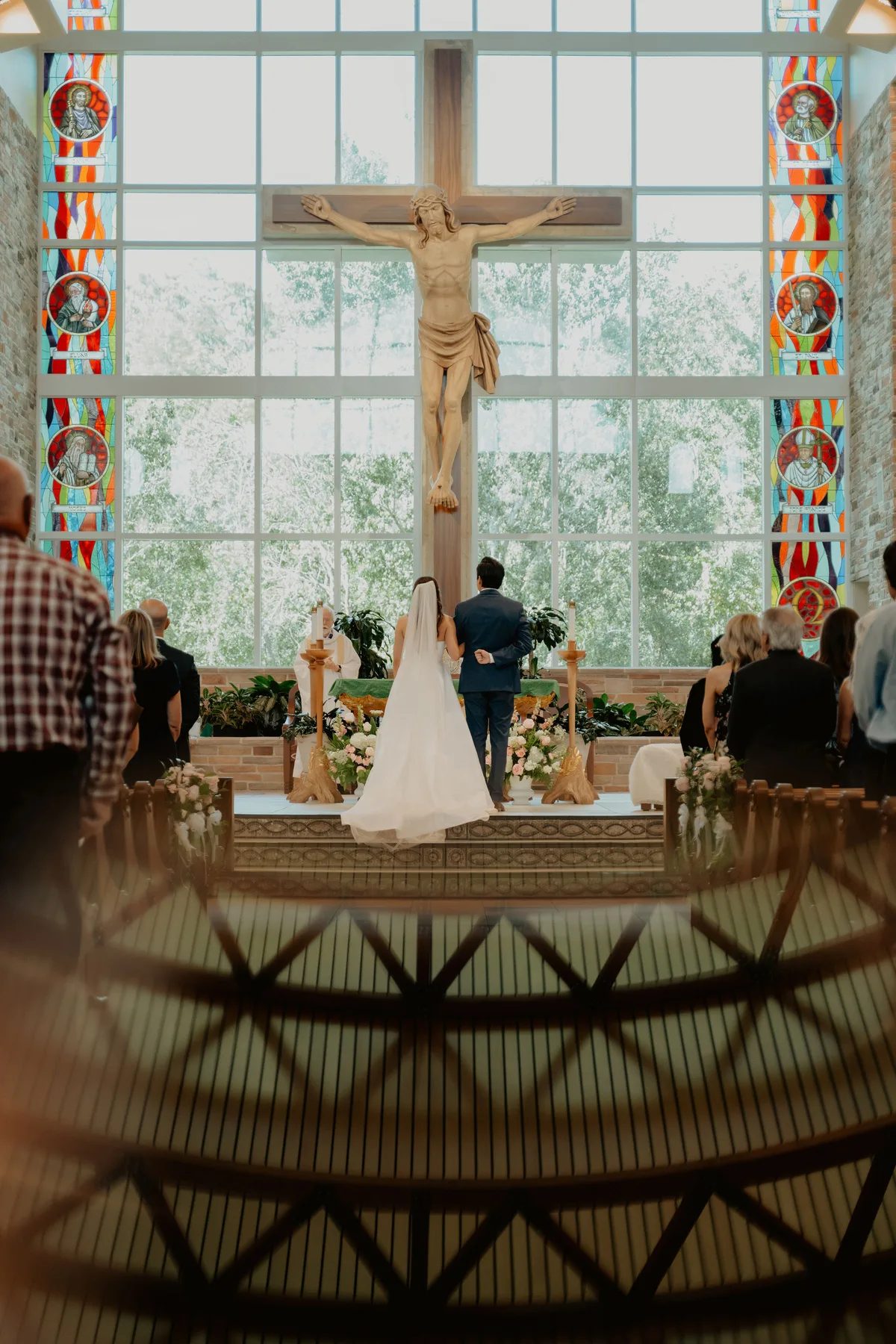 A man and woman stand before a cross with their wedding party behind them.