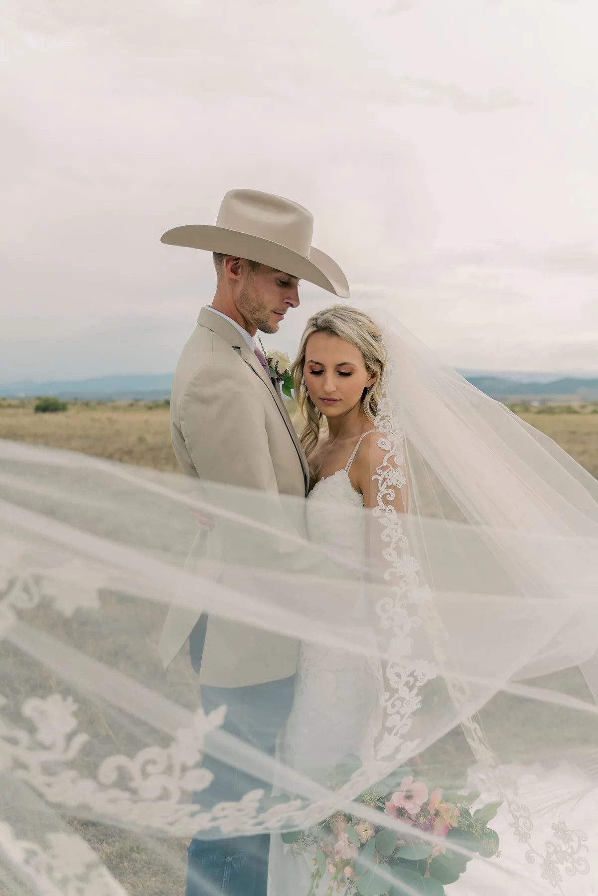 A bride and groom share a tender moment under an expansive sky in a rural setting.