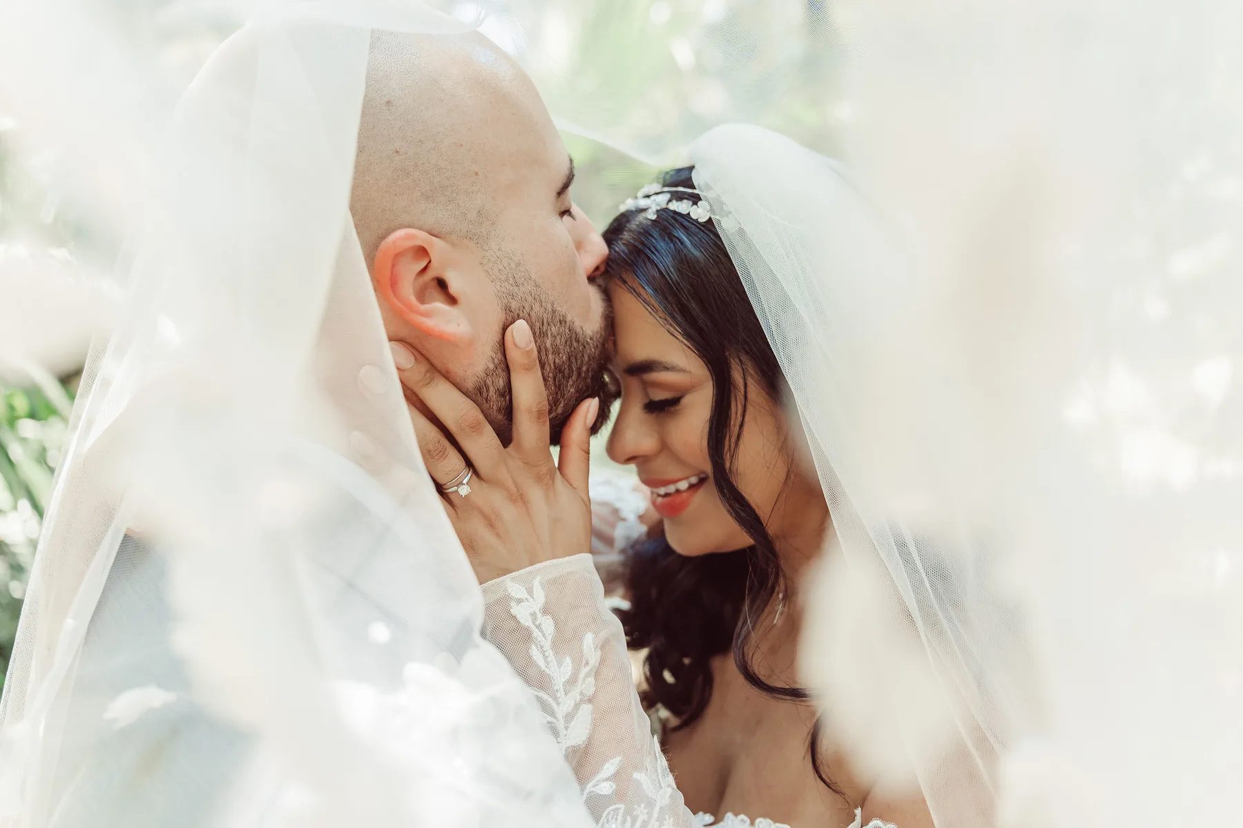 A tender moment captured between a bride and groom under their wedding veil in an outdoor garden setting.