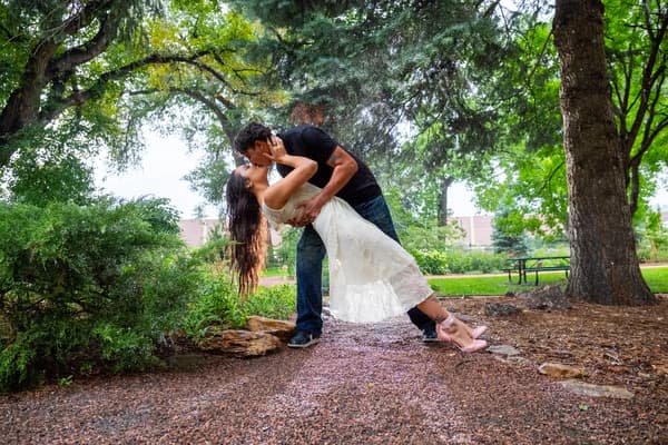 A couple shares an intimate kiss amidst a shower of rain in a lush outdoor garden setting.