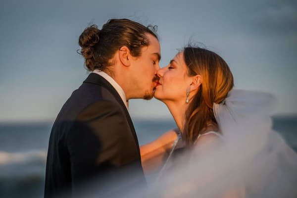 A man with a ponytail kisses the bride on her forehead.