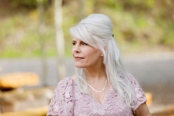 A woman with white hair wearing a pink dress stands by the roadside.