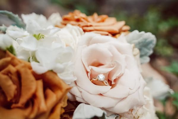 A bouquet of flowers with a pink rose that has a diamond ring on it.