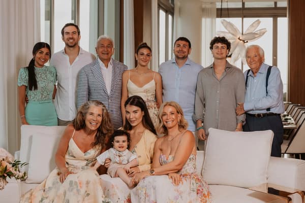 A group of people posing for a photo with their child on the lap. The room they are in has white walls and windows. The atmosphere is happy and joyful as everyone smiles for the camera.