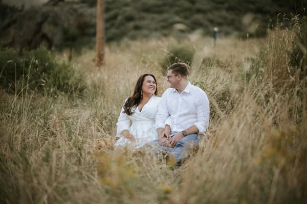 A couple shares a joyful moment in tall grass during golden hour.
