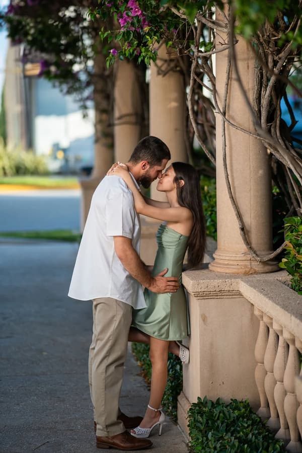 A couple shares an intimate moment against a backdrop of lush greenery and classical architecture during golden hour.