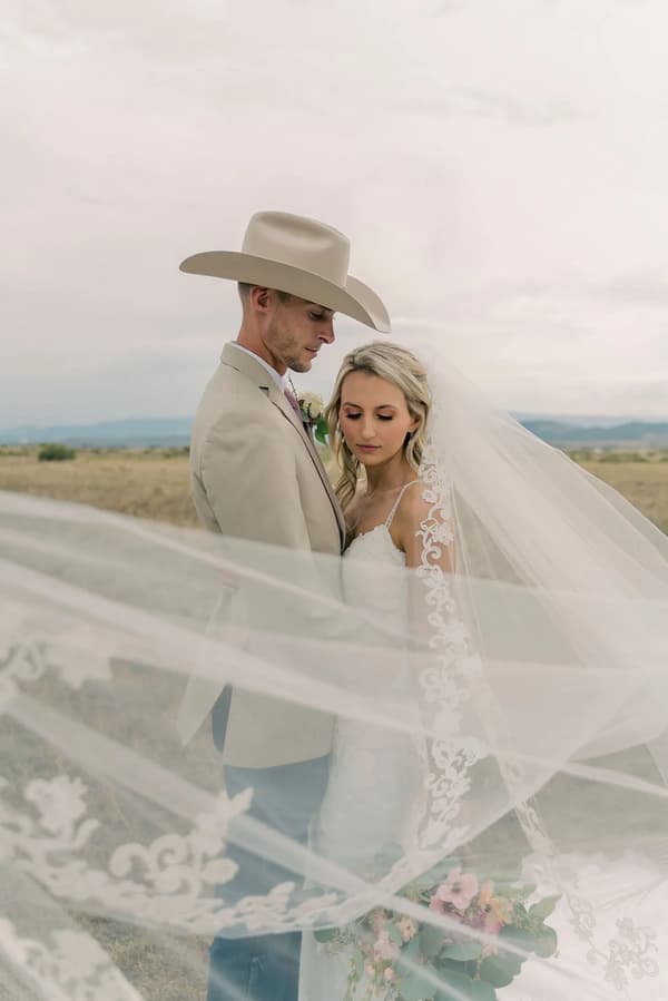 A bride and groom share a tender moment under an expansive sky in a rural setting.
