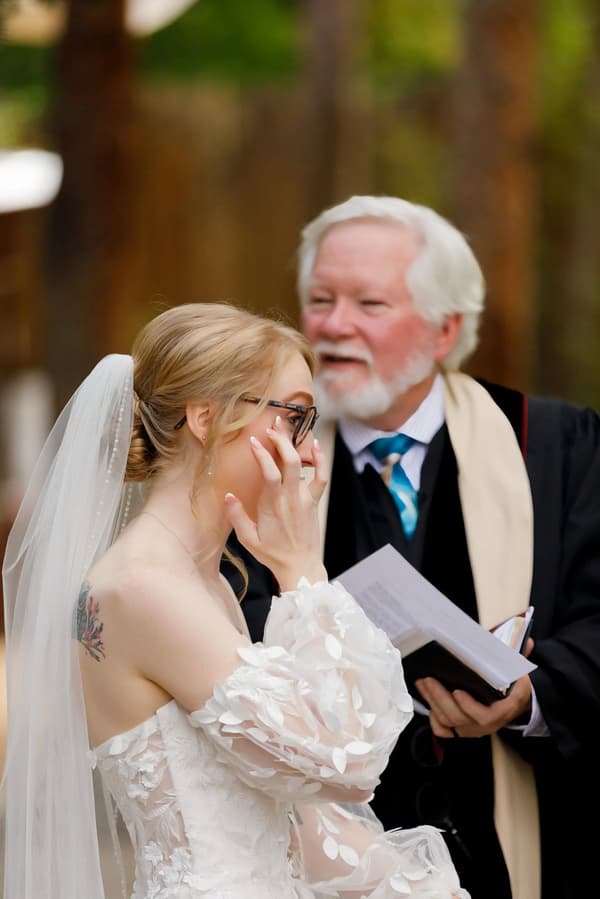 A bride is talking on her cell phone while a man looks at her with a smile on his face.